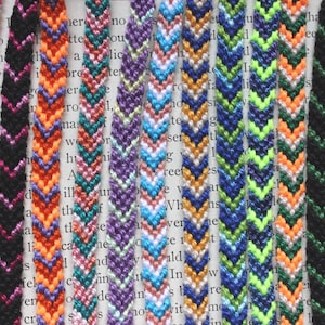 May include: A collection of colorful friendship bracelets with chevron patterns. The bracelets feature various color combinations, including pink, black, orange, teal, purple, blue, and green. Each bracelet is approximately 0.5 inches wide.