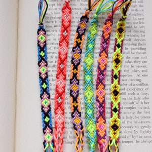 May include: A set of six colorful friendship bracelets with a diamond pattern. The bracelets are made with bright neon colors, including pink, orange, yellow, green, blue, and purple.