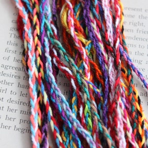 May include: A close-up of a bundle of colorful embroidery floss, with a variety of colors and textures. The floss is arranged in a loose, flowing pattern, creating a visually appealing and vibrant display.