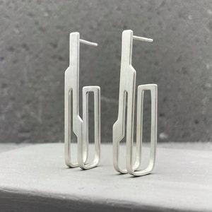 May include: A pair of silver geometric earrings with a modern design. The earrings are made of two rectangular shapes, one inside the other.
