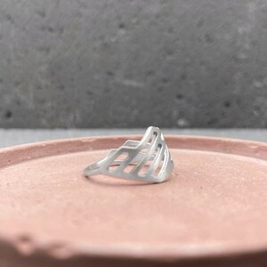 Pode incluir: Um anel de prata com um design geom&eacute;trico. O anel &eacute; feito de um metal fino e tem um design delicado e vazado.