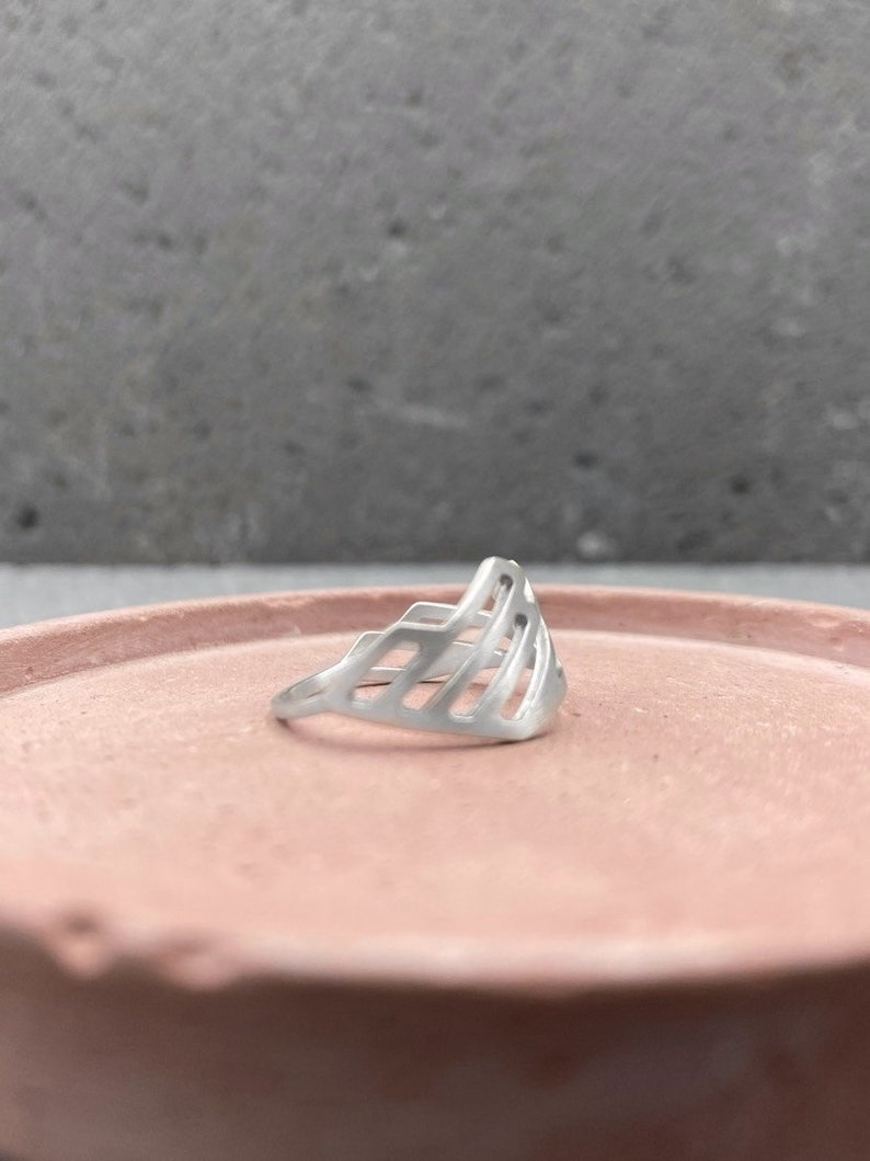 Pode incluir: Um anel de prata com um design geom&eacute;trico. O anel &eacute; feito de um metal fino e tem um design delicado e vazado.