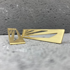Peut inclure: Une paire de boucles d'oreilles dorées avec un motif géométrique. Les boucles d'oreilles sont en métal et ont une finition brossée.