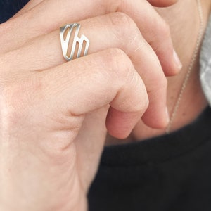 Pode incluir: Um anel de prata com um design geom&eacute;trico. O anel est&aacute; no dedo de uma pessoa.