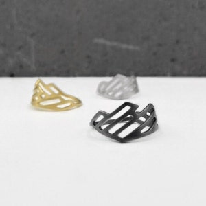 Pode incluir: Tr&ecirc;s an&eacute;is geom&eacute;tricos em ouro, preto e prata. Os an&eacute;is s&atilde;o de metal e t&ecirc;m um design geom&eacute;trico.