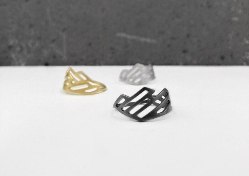 Pode incluir: Tr&ecirc;s an&eacute;is geom&eacute;tricos em ouro, preto e prata. Os an&eacute;is s&atilde;o de metal e t&ecirc;m um design geom&eacute;trico.