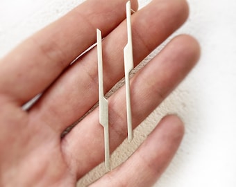May include: A pair of silver earrings with a geometric design. The earrings are long and thin, with a sharp angle at the top.