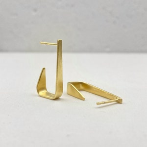 May include: A pair of gold-toned geometric earrings with a brushed finish. The earrings are shaped like a hook with a pointed end.