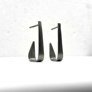 May include: A pair of silver hoop earrings with a unique, slightly curved, open design.