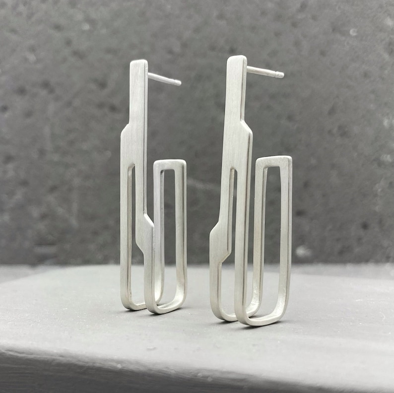 May include: A pair of silver geometric earrings with a modern design. The earrings are made of two rectangular shapes, one inside the other.