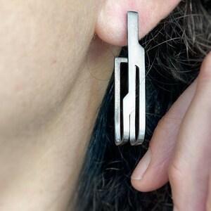 May include: Silver geometric dangle earrings with a modern design. The earrings are made of multiple thin metal strips that are connected to form a unique shape.