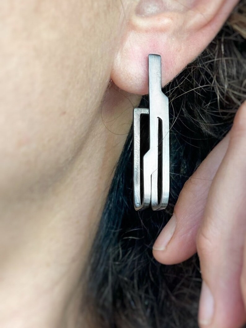 May include: Silver geometric dangle earrings with a modern design. The earrings are made of multiple thin metal strips that are connected to form a unique shape.