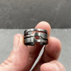 May include: A silver ring with a geometric design. The ring is made of multiple bands that are stacked on top of each other.