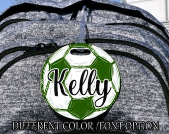May include: A green and white soccer ball luggage tag with the name "Kelly" written in black cursive font.