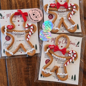 May include: Three gingerbread person ornaments made of tan braided cord, each featuring a red bow, a red heart labeled 2026, a candy cane, and white icing accents. Each ornament is personalized with white letter beads spelling Camryn, Owen, or Anthony.