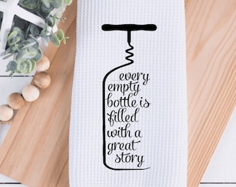 May include: White kitchen towel with a black silhouette of a corkscrew and the text "every empty bottle is filled with a great story".