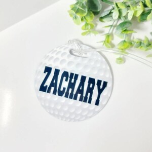 Peut inclure: Etiquette &agrave; bagages en forme de balle de golf blanche avec le nom Zachary imprim&eacute; en noir.