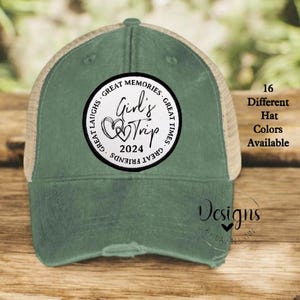 May include: A green and tan trucker hat with a white circle patch that says "Girl's Trip 2024" with hearts and the text "Great Memories, Great Times, Great Laughs, Great Friends". The hat is distressed and has a mesh back.