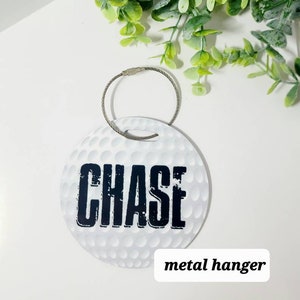 Peut inclure: Etiquette &agrave; bagages ronde blanche avec un motif de balle de golf et le nom "CHASE" imprim&eacute; en noir. L'&eacute;tiquette est munie d'un crochet m&eacute;tallique.