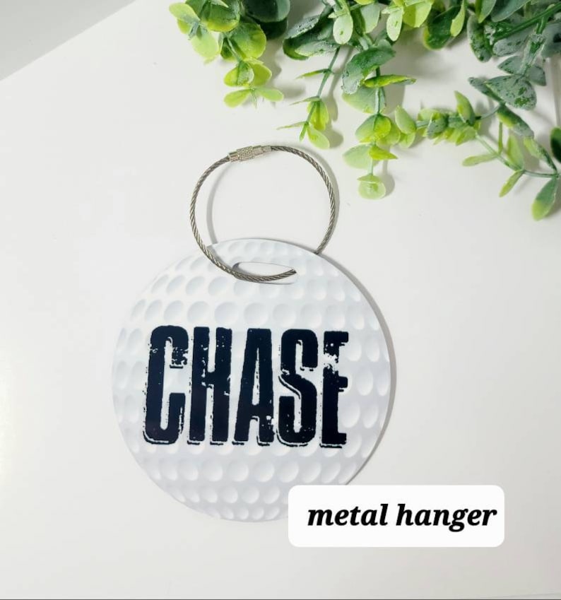 Peut inclure: Etiquette &agrave; bagages ronde blanche avec un motif de balle de golf et le nom "CHASE" imprim&eacute; en noir. L'&eacute;tiquette est munie d'un crochet m&eacute;tallique.