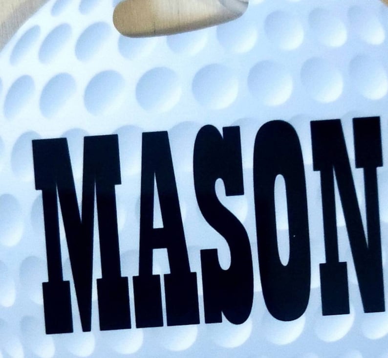 Peut inclure: Une balle de golf blanche avec une surface &agrave; picots noirs. Le nom "MASON" est imprim&eacute; en grandes lettres noires sur la balle.