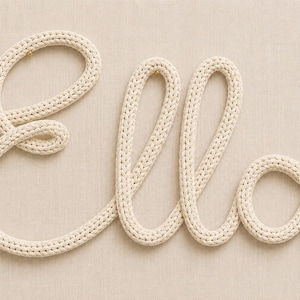 May include: A wall-mounted decorative sign featuring the name Ella written in a continuous cursive script. The letters are formed from a thick, off-white knitted cord with a visible braided texture, creating a soft, three-dimensional appearance.
