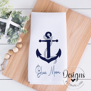 May include: White kitchen towel with a blue anchor and rope design. The text "Blue Moon Designs by Dawn Lynn" is printed below the anchor.