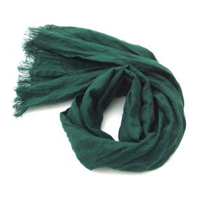 Peut inclure: Une écharpe vert foncé avec une bordure effilochée, drapée sur fond blanc. Le tissu est doux et fluide, avec une texture et des plis visibles. La couleur est une nuance de vert riche et profonde.