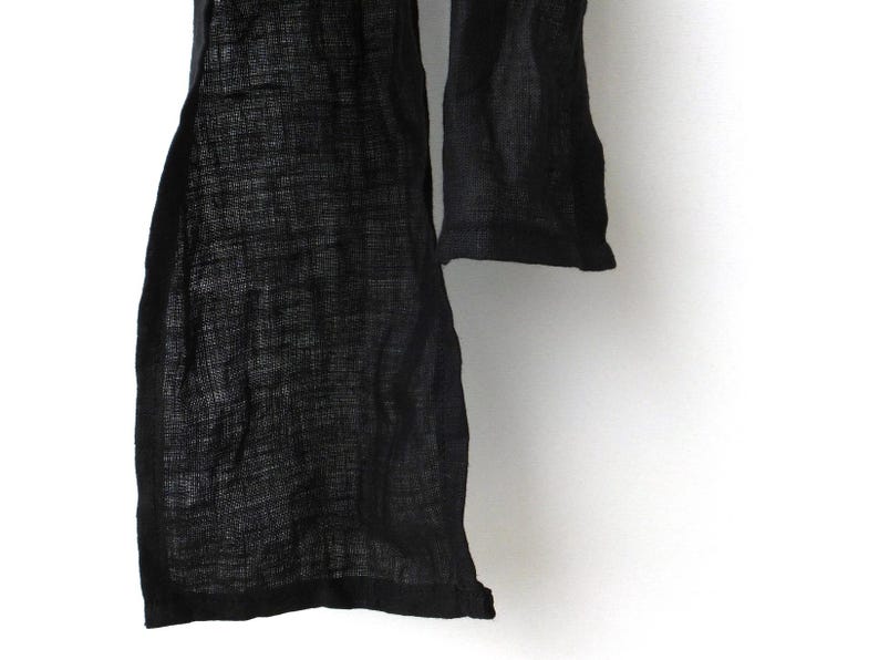 Close-up of lain hemmed ends of a narrow black linen scarf.