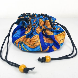 Puede incluir: Una pequeña bolsa de cordón azul y naranja con un cordón negro y cuentas de madera. La bolsa está hecha de tela con un patrón geométrico.