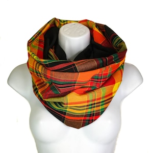May include: A vibrant plaid infinity scarf in red, orange, yellow, green, and black. The scarf is displayed on a white mannequin, highlighting its circular design. The fabric appears to be a lightweight material.