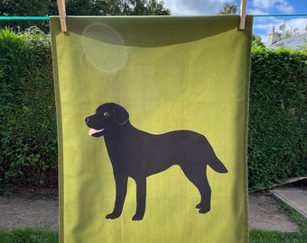 May include: A green tea towel featuring a black silhouette of a Labrador Retriever dog.