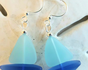 May include: A pair of silver earrings featuring blue and light blue sea glass in the shape of a sailboat.