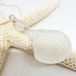 May include: A white sea glass shell pendant necklace with a white bead and silver chain.