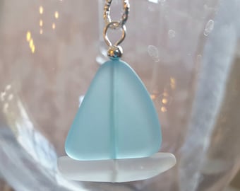 May include: A light blue glass sailboat pendant necklace with a silver chain. The sailboat is made of sea glass and has a white sail.