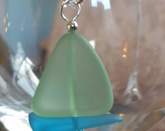 May include: A light blue and green glass sailboat pendant necklace. The sailboat is made of two pieces of glass, one for the sail and one for the hull. The pendant is attached to a silver chain.