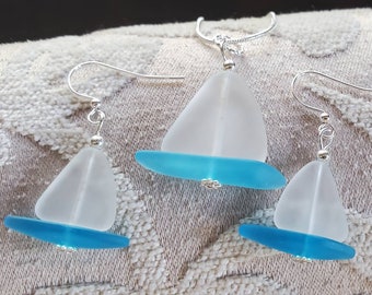 May include: A set of sea glass earrings and a necklace featuring a sailboat design. The sail is made of frosted white sea glass and the hull is made of turquoise sea glass.