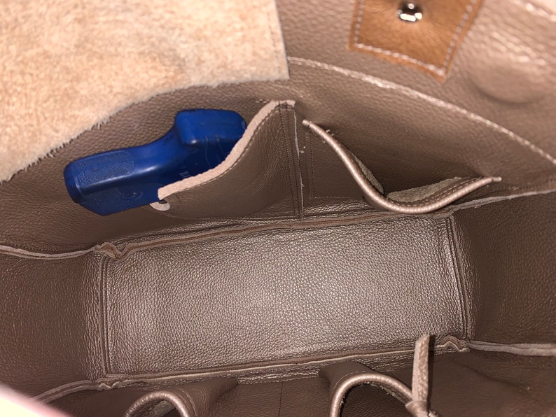 May include: The inside of a brown leather bag with multiple pockets. A blue handgun is visible in one of the pockets.