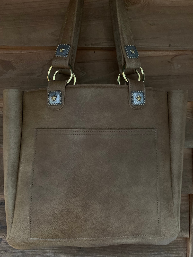 May include: A brown leather tote bag with a large pocket on the front. The bag has two top handles with gold rings and star-shaped accents.