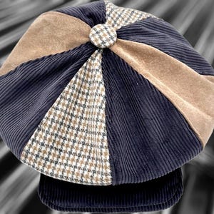 May include: A multi-paneled newsboy cap featuring alternating sections of navy blue corduroy, tan suede-like fabric, and a brown and white houndstooth pattern. The cap is topped with a central button covered in the same houndstooth fabric.