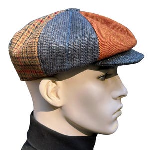 May include: A multi-paneled flat cap featuring a patchwork design with sections of brown plaid, blue textured fabric, and orange herringbone wool. The cap has a rounded crown and a short, stiff brim, constructed from various woven textile patterns.