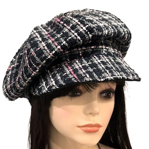 May include: A newsboy cap featuring a textured tweed fabric in a dark navy blue, black, and white plaid pattern with thin, vertical and horizontal pink thread accents woven throughout. The cap has a rounded, full crown and a short, stiff brim.