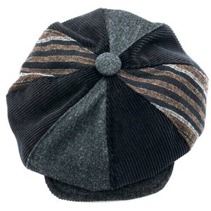 Puede incluir: Una gorra de estilo newsboy de varios paneles con un diseño de patchwork que combina pana negra, lana afieltrada gris carbón y tela a rayas marrones y negras. La gorra presenta un botón central forrado en tela y una visera de lana gris oscuro.