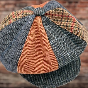 May include: A multi-panel newsboy cap constructed from various fabric textures and patterns, including a central orange herringbone panel, blue denim-like sections, and brown plaid tweed segments with thin red and green accent lines.