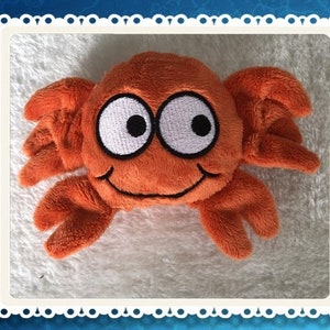 Op de afbeelding: Oranje pluche krab speelgoed met grote witte ogen en een glimlachende mond.