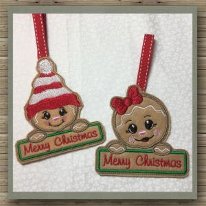 May include: Two gingerbread person ornaments with red and white striped hats and bows. Each ornament holds a sign that says "Merry Christmas" in green letters.