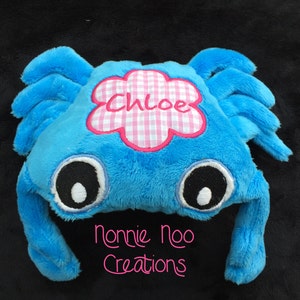 Pode incluir: Brinquedo de pelúcia azul em forma de caranguejo com olhos bordados e uma flor de vichy rosa e branca com o nome "Chloe" bordado nela. O brinquedo é feito por "Nonnie Noo Creations".