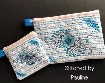 Op de afbeelding: Twee gestikte ritszakjes met een roze en blauw ruitjespatroon en blauwe bloemenborduursel. De zakjes zijn van verschillende grootte. Het grotere zakje ligt bovenop het kleinere zakje. De tekst "Stitched by Pauline" staat onder de zakjes.