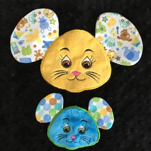 May include: Two plush toy mice with embroidered faces. The larger mouse is yellow with white and blue patterned ears. The smaller mouse is blue with green and brown patterned ears.