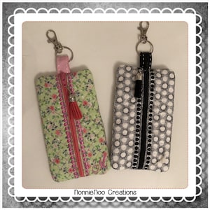 Puede incluir: Dos bolsas con cremallera con llaveros. Una bolsa es verde con un estampado floral y una cremallera rosa. La otra bolsa es blanca y negra con lunares y una cremallera negra. Ambas bolsas tienen un borla.